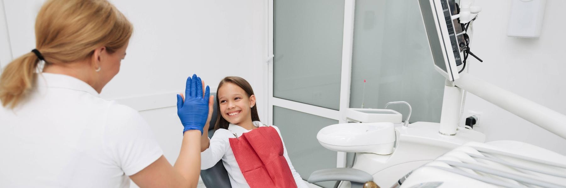 Young girl sitting in dental chair giving her dentist a high five after cleaning in Randolph, NJ